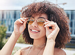 Portrait of young trendy beautiful mixed race woman with an afro smiling and posing alone outside. Hispanic woman wearing sunglasses and feeling happy. Fashionable african american woman in the city