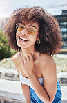 Portrait of young trendy beautiful mixed race woman with an afro smiling and posing alone outside. Hispanic woman wearing sunglasses and feeling happy. Fashionable african american woman in the city