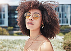 Cool, trendy african american woman with a curly afro wearing sunglasses outside. Face of a young serious mixed race woman enjoying a summer day while standing outside. Hipster girl in the city