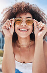 Portrait of young trendy beautiful mixed race woman with an afro smiling and posing alone outside. Hispanic woman wearing sunglasses and feeling happy. Fashionable African American woman in the city