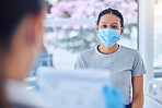 Mixed race patient wearing a mask in consult with a doctor. Doctor checking a patients chart on a clipboard. Doctor holding a clipboard in a checkup. Patient in covid checkup with physician.