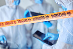 Closeup on biohazard quarantine tape. Hands of scientist using a digital tablet behind covid barrier. Medical professional working in a biohazard crime scene. Doctors working behind caution tape