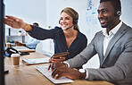 Happy caucasian female call centre telemarketing agent discussing plans with african american colleague while working together on computer in an office. Two consultants troubleshooting solution for customer service and sales support