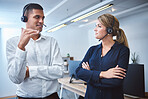 Mixed race call centre telemarketing agent discussing plans with caucasian colleague while working together in an office. Two consultants troubleshooting solution for customer service and sales support