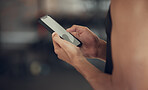 Hands of a man sending a text on his smartphone in the gym. Man taking a break from exercise to use his cellphone. Screen of a mobile phone being used in the gym.Man using a cellphone cropped