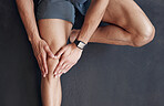 Closeup of one mixed race man from above holding his sore knee while exercising in a gym. Guy suffering with painful leg injury from fractured joint and inflamed muscles during workout. Struggling with stiff body cramps causing discomfort and strain