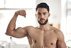 Portrait of one fit young hispanic man flexing his biceps to show big strong muscles from regular exercise in a gym. Serious bodybuilder with toned arms and sexy physique. Topless athlete proud of physical progress and powerful form