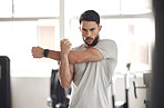 Portrait of one fit young hispanic man stretching arms and shoulders for warmup to prevent injury while exercising in a gym. Serious muscular guy focused on staying motivated and determined while mentally and physically preparing for training workout