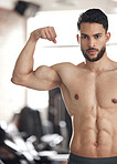 Portrait of one fit young hispanic man flexing his biceps to show big strong muscles from regular exercise in a gym. Serious bodybuilder with toned arms and sexy physique. Topless athlete proud of physical progress and powerful form