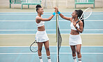 Two professional tennis players laughing after a match. Young african american girls high five by the tennis net on the court. Cheerful tennis players standing on the court