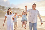 Cute little girl swinging while holding hands with her parents. Young mom and dad walking hand in hand with their daughter and lifting her while walking on the beach. Family fun in the summer sun