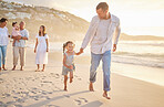 Cute little girl running hand in hand with her mixed race dad on the beach. A daughter and her father holding hands while playing in the sand next to the sea at sunset. Family bonding at the coast