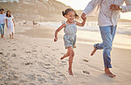 Cute little girl running hand in hand with her mixed race dad on the beach. A daughter and her father holding hands while playing in the sand next to the sea at sunset. Family bonding at the coast