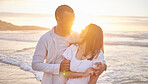 Affectionate young mixed race couple sharing an intimate moment on the beach. Happy husband and smiling wife enjoying a summer day by the sea. They love spending time together on the coast at sunset