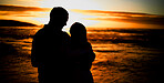 Silhouette affectionate young couple sharing an intimate moment on the beach. Backlit happy husband and wife enjoying a summer day by the sea. They love spending time together on the coast at sunset