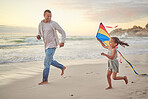 Cute little girl and her mixed race dad flying a kite on the beach. Adorable daughter and her handsome father running and playing in the sand next to the sea at sunset. Family bonding and happiness