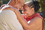 Happy affectionate mature african american couple sharing an intimate moment outside at the park during summer. In love seniors smiling and embracing while spending quality time together outdoors