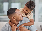 Handsome young mixed race man and his adorable son hugging on a sofa in the living room at home. Father and his boy child bonding and showing affection. A single parent and his male kid in the lounge