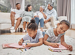 Two cute mixed race sibling sisters drawing and colouring in in the living room with their parents and grandparents in the background. Carefree kids playing while mom, dad, granny and grandpa look on