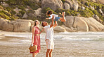 Full length of a happy mixed race family enjoying family time together at the beach. Loving father lifting his daughter in the air and having fun by the sea while her mother watch. Young couple enjoying vacation by the beach with their little girl