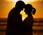 Silhouette affectionate senior couple sharing an intimate moment on the beach. Backlit happy husband and wife enjoying a summer day by the sea. They love spending time together on the coast at sunset