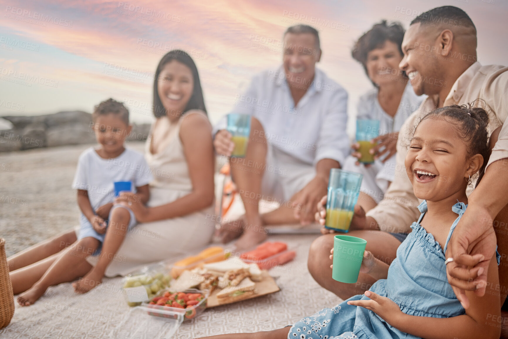 Buy stock photo Happy family, beach and kid laughing at picnic for holiday, summer or travel. Lunch, food and people by sea with parents, generations or funny children drink juice at thanksgiving celebration outdoor