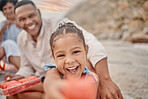 Portrait of a little hispanic girl having a snack while on a picnic with her family at the beach. Mixed race girl having fun with her family and having snacks