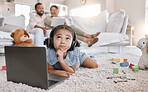 Closeup of a little cute girl using a laptop and wireless headphones while laying on the floor in the lounge. Hispanic girl using a wireless device to do her homework in the living room