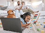 Closeup of a little cute girl using a laptop and wireless headphones while laying on the floor in the lounge. Hispanic girl using a wireless device to do her homework in the living room