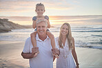 Portrait of a little caucasian girl being carried by her grandpa while her mother walks on the beach during sunset.  Family fun in the summer sun