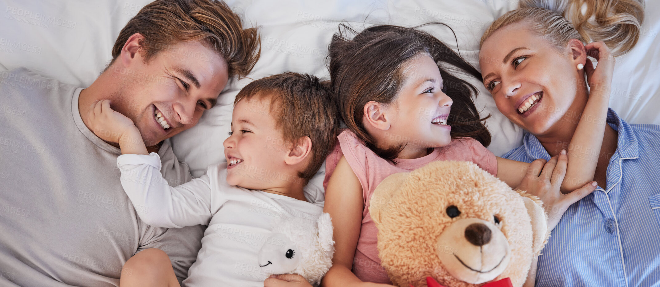 Buy stock photo Happy, family and above with embrace in bedroom for love connection, bonding and support of childhood memory. Smile, parents and girl with teddy bear, hug and relax together for morning care at house