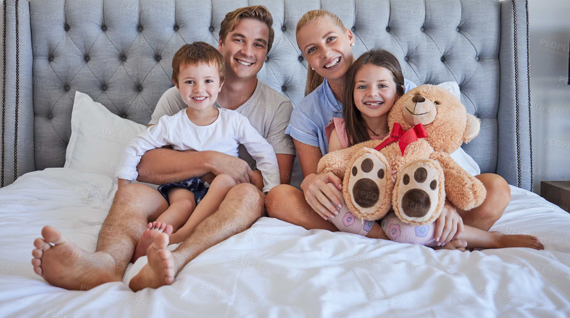 Buy stock photo Portrait, family and smile with embrace in bedroom for love, bonding and weekend support of childhood memory. Happy, parents and kids with teddy bear, hug and relax together for morning care at house