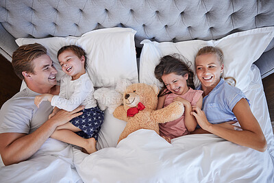 Buy stock photo Above, family and laughing with love in bedroom for funny joke, bonding and tickling game of embrace support. Happy, parents and girl with teddy bear, hug and comic together for morning care at house