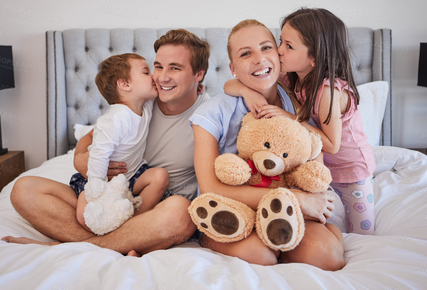 Buy stock photo Happy, family and embrace with kiss in bedroom for love, bonding and childhood support of memory. Smile, parents and kids with teddy bear, hug and relax together for relationship connection at house