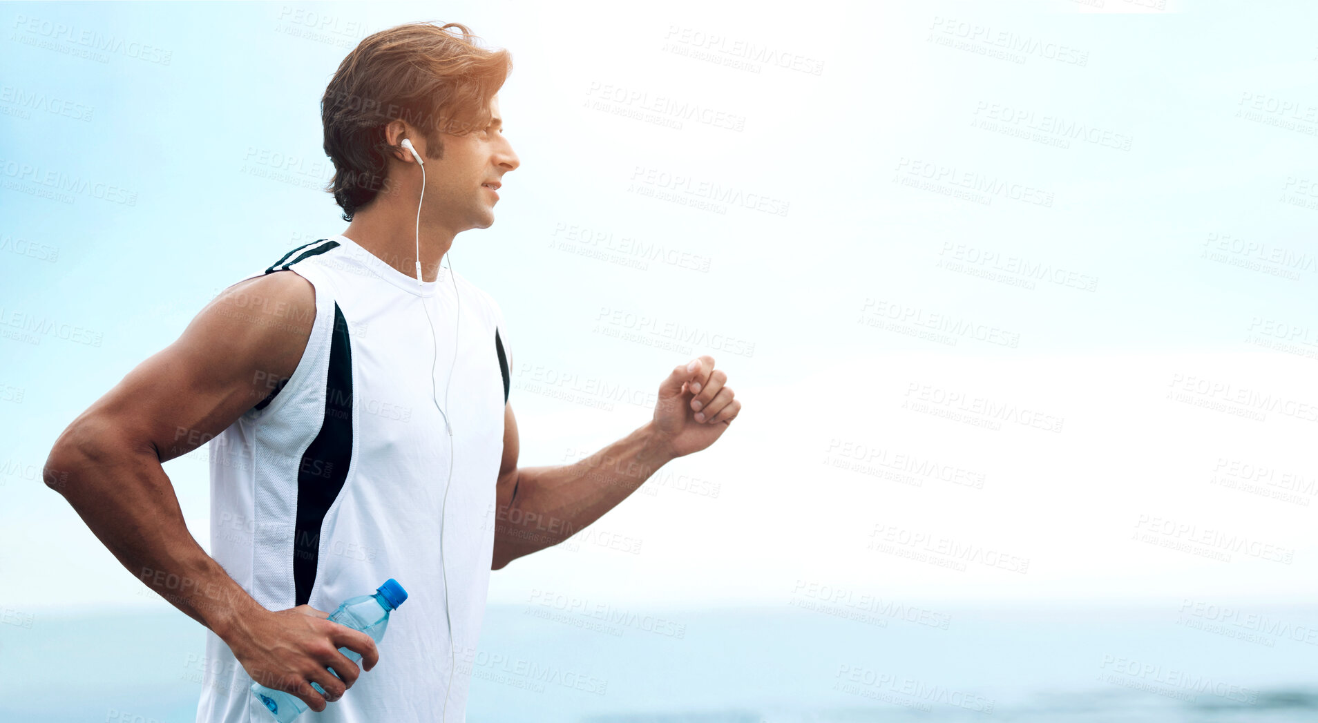 Buy stock photo Profile view of a handsome man holding a water bottle, going for a run and listening to music - copyspace