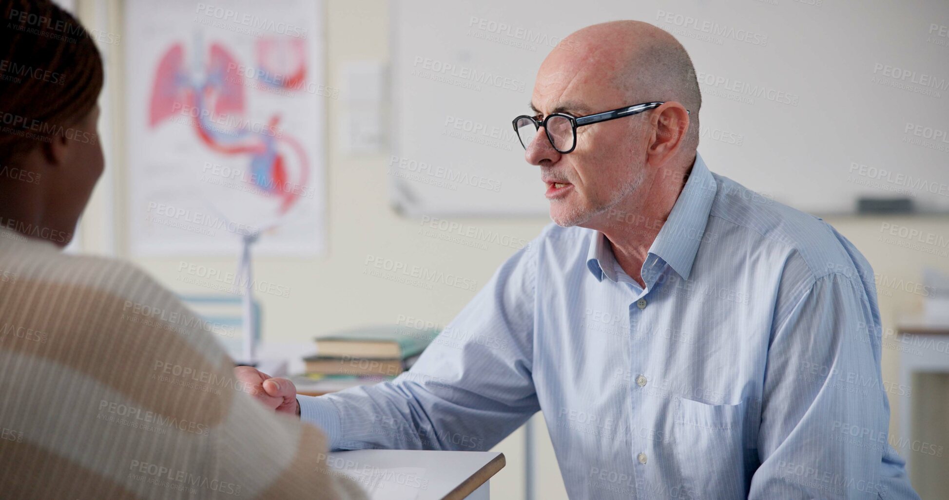 Buy stock photo Man, teacher and student at desk for education, question and help with information in classroom. Male tutor, person and discussion at table for shared knowledge, life science lesson and assistance