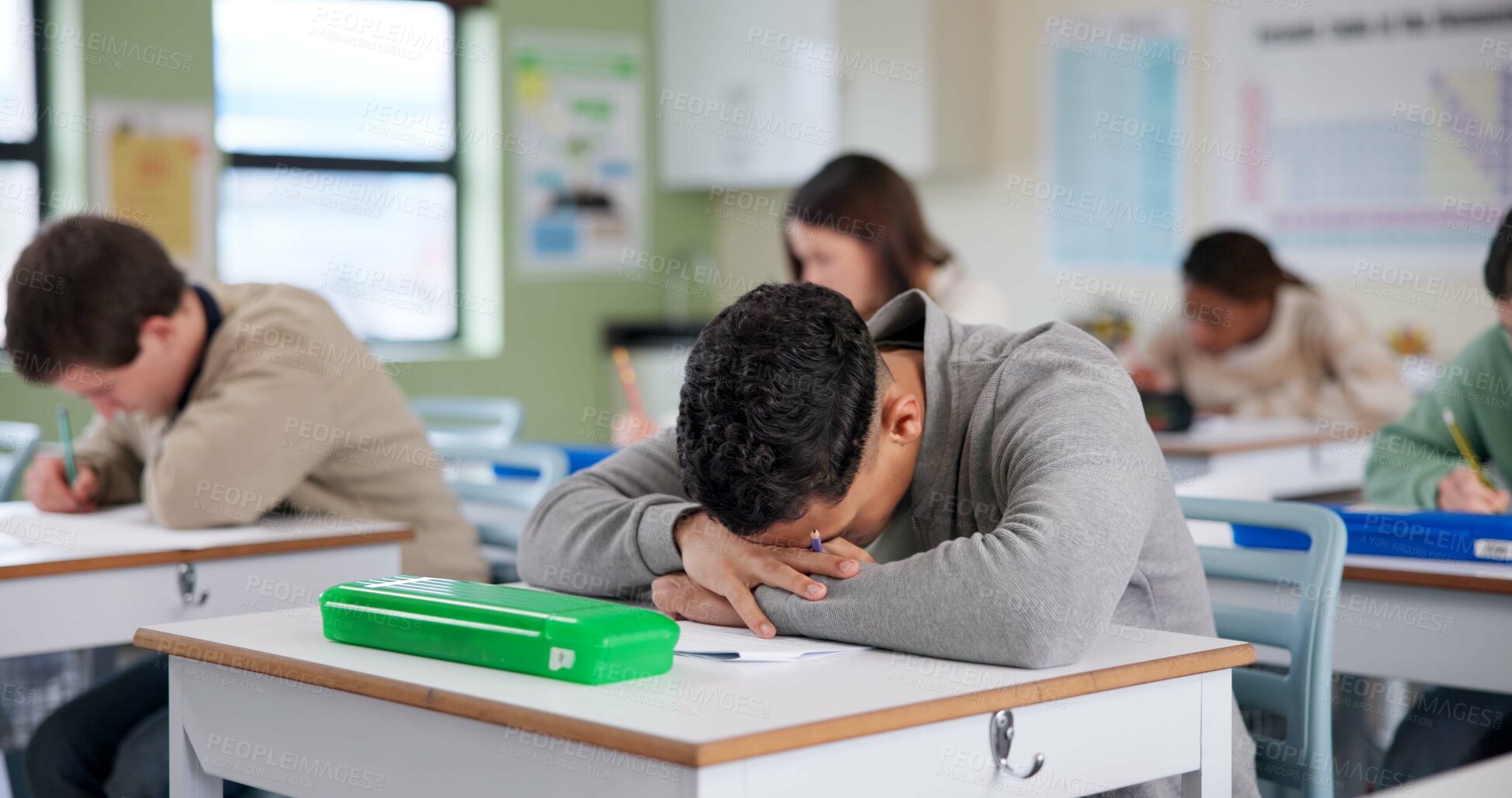 Buy stock photo Exam, boy and tired on desk with stress, overwhelmed and brain fog in classroom. Student, depression and overthinking in test with anxiety, burnout and mental health fatigue in high school lesson 