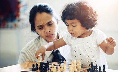 Buy stock photo A cute little girl playing chess while her mom looks on