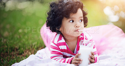 Buy stock photo Adorable little girl drinking milk through a straw while lying on the grass