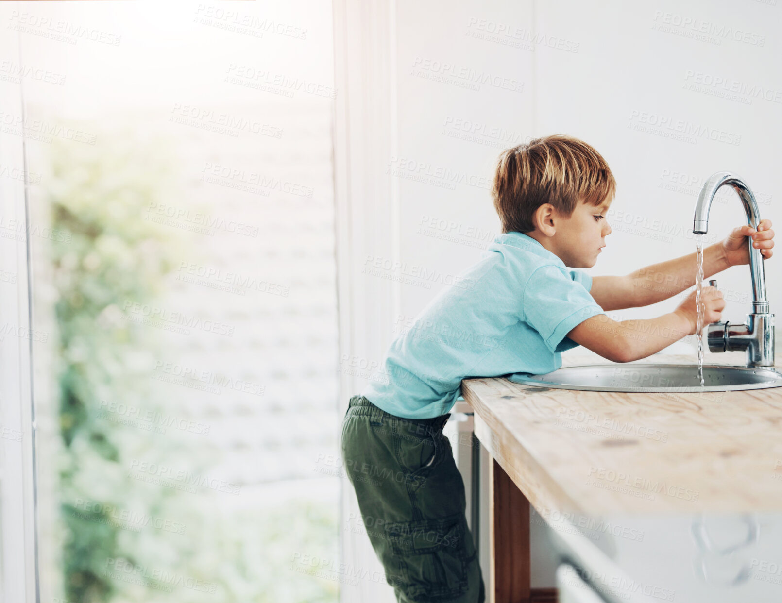 Buy stock photo A cute young boy climbing the kitchen counter to get to the tap