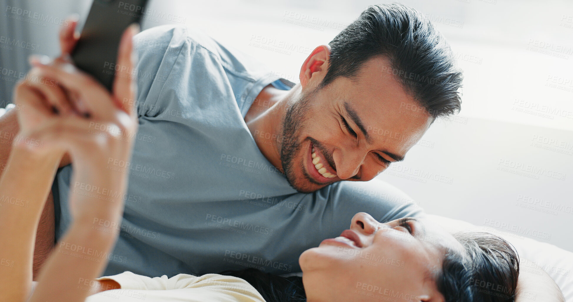 Buy stock photo Happy couple, relax and laughing with phone on bed for funny morning, social media or comedy at home. Man or woman with smile lying in bedroom on mobile smartphone for humor or joke together at house