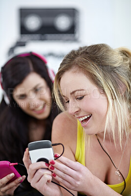 Buy stock photo Two young female friends listening to music on a mp3 player together