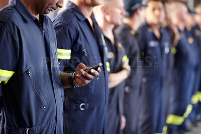 Buy stock photo A fireman using his cellphone while standing in a row with his colleagues