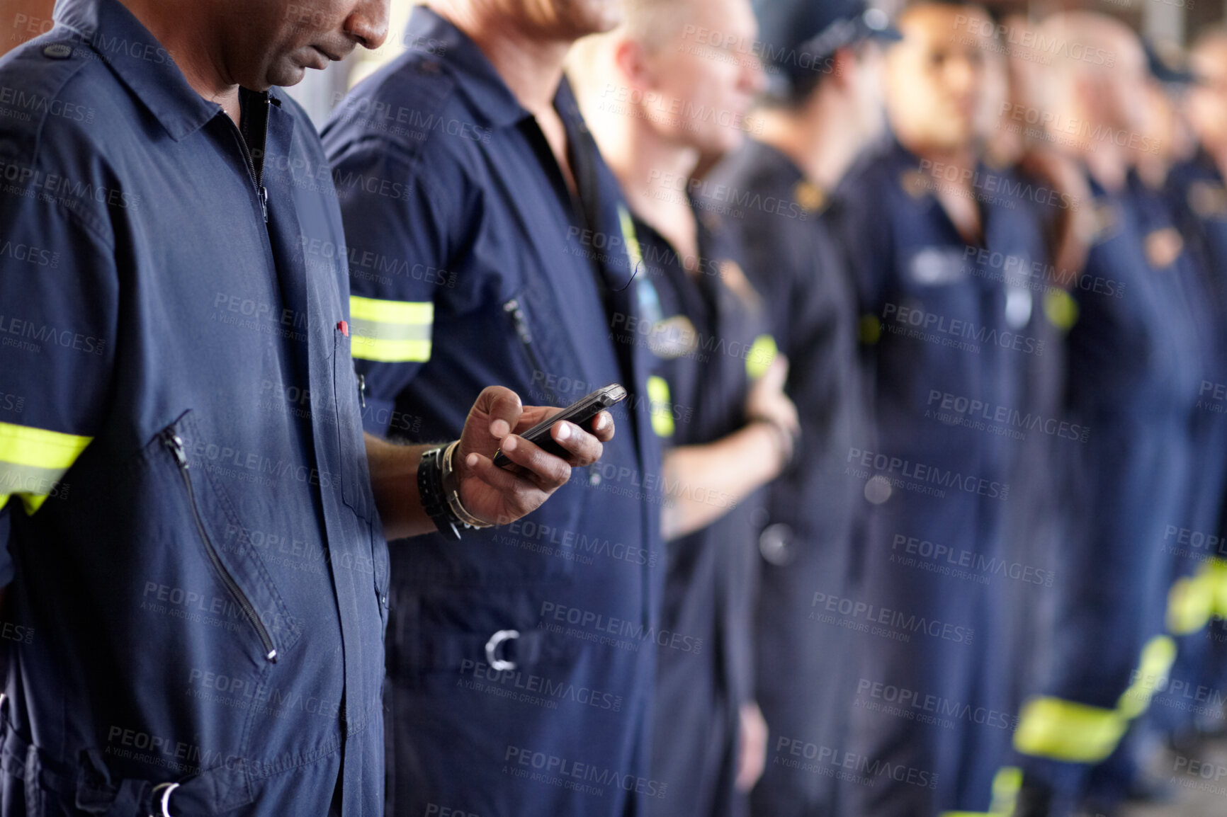 Buy stock photo A fireman using his cellphone while standing in a row with his colleagues