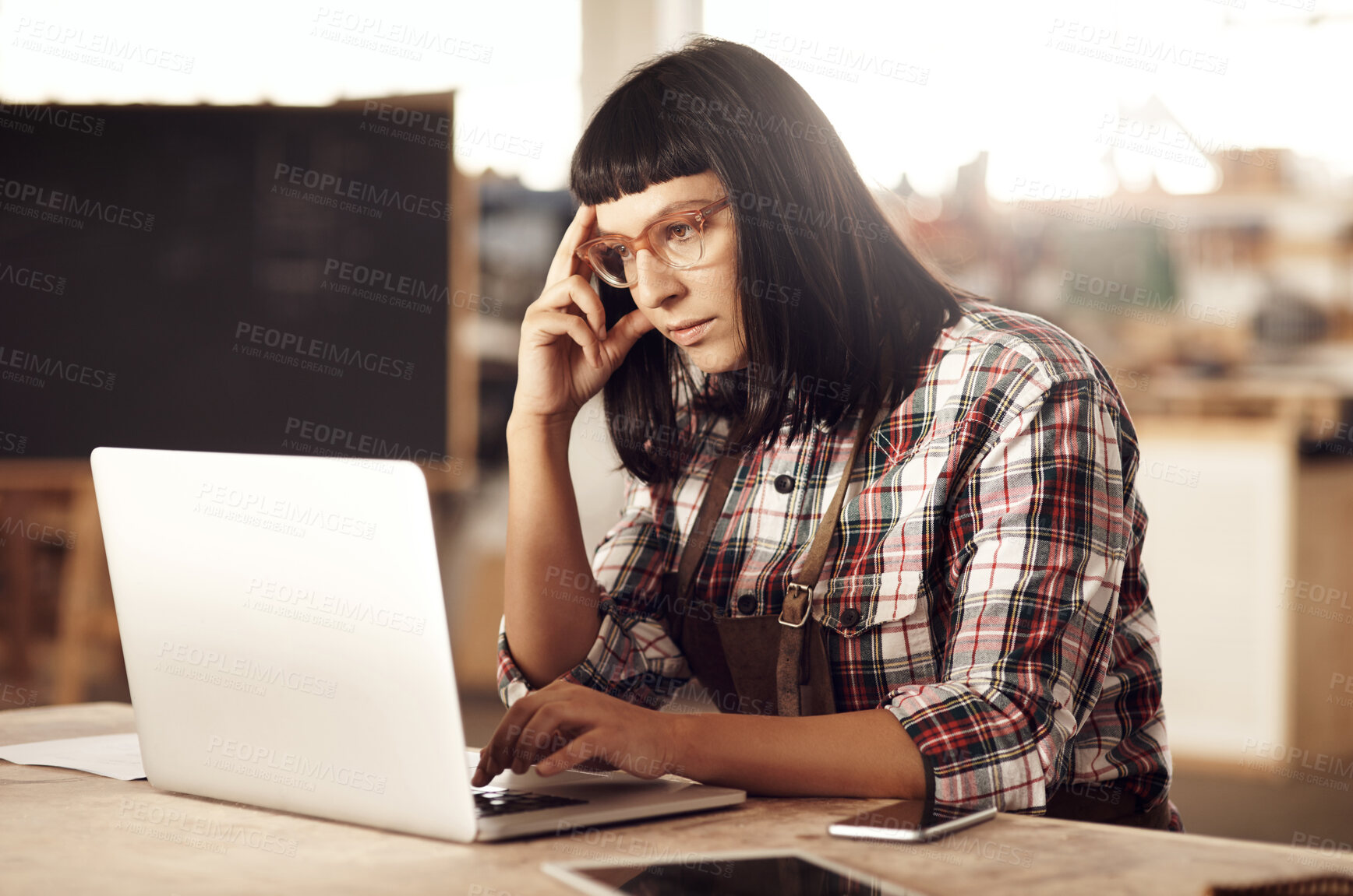 Buy stock photo Cropped shot of an attractive young woman working on her laptop while sitting in her creative workshop