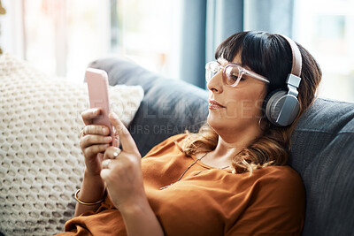 Buy stock photo Woman, home and smartphone with headphones on sofa for streaming music in website. Female person, living room and couch with online subscription for podcast, audio and radio to rest, relax and break