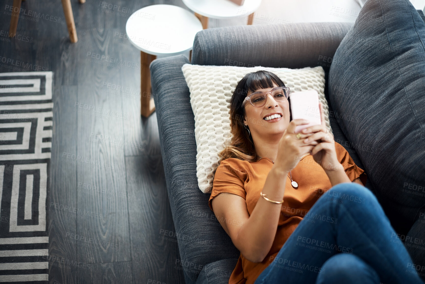 Buy stock photo Above, woman and rest with phone on sofa for communication, social media and reading ebook. Smile, female person and relax with glasses on mobile, online news and typing email for texting at house