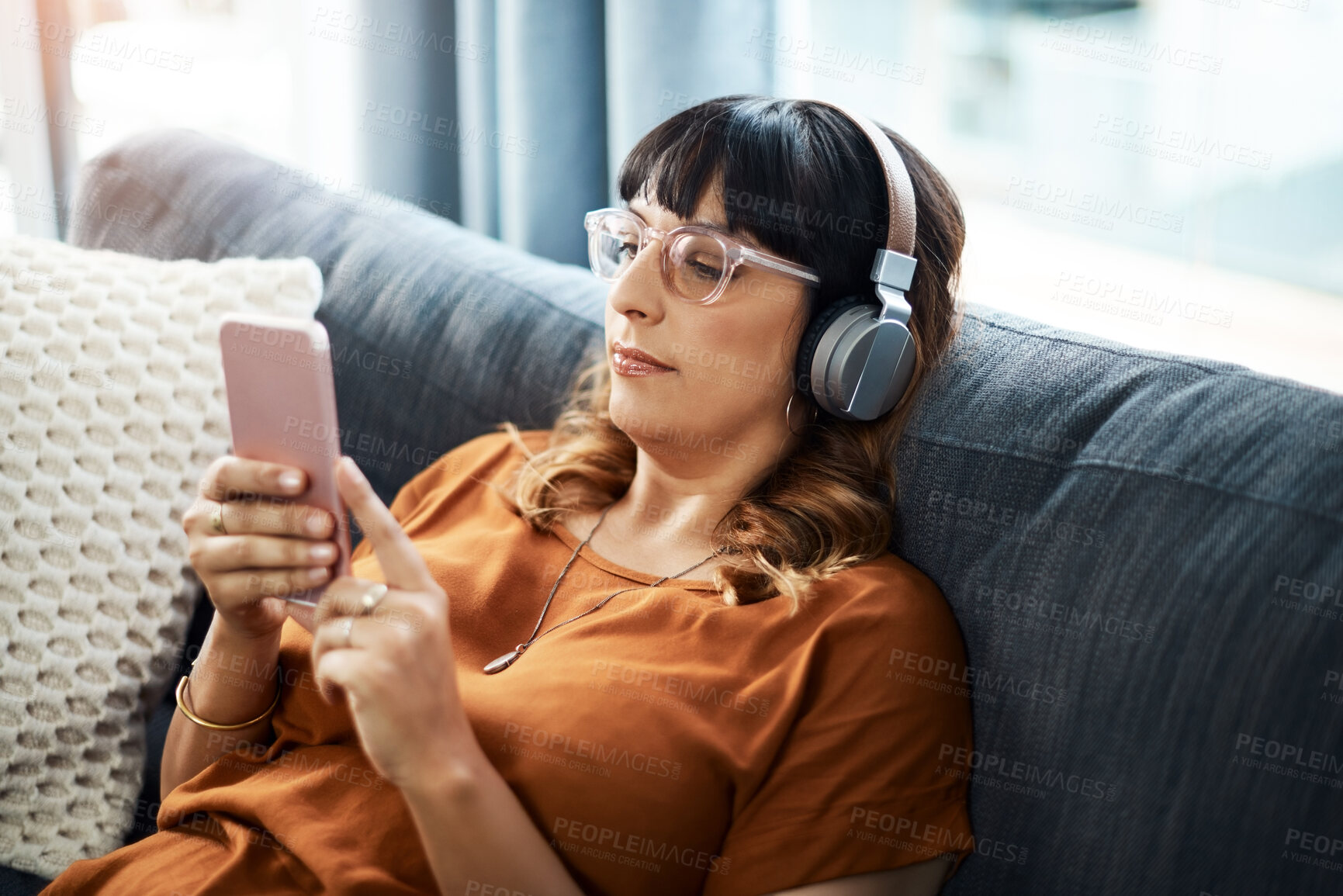 Buy stock photo Woman, house and smartphone with headphones on sofa for streaming music in website. Female person, living room and couch with online subscription for podcast, audio and radio to rest, relax and break