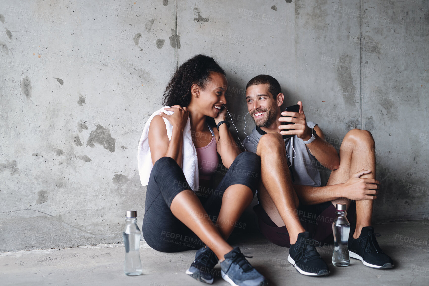 Buy stock photo Man, woman and training rest with phone for fitness podcast, streaming in building for wellness. Couple, mobile app or workout together with break in parking lot for health, music for gym or exercise