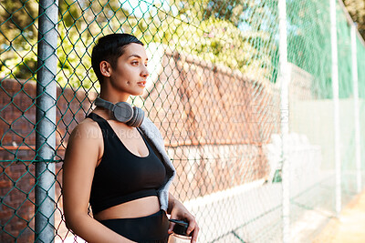 Buy stock photo Shot of a sporty young woman taking a break while standing against a fence outdoors